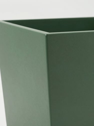 Close-up of a craftsman finishing a large-scale custom matte forest green planter, highlighting the textured finish and clean architectural lines.