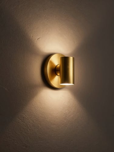Moody editorial photography of a minimalist matte brass vanity sconce on raw plaster, casting a warm ambient glow, deep shadows, 50mm