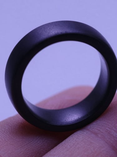 Macro close-up of a sleek, matte-black biometric ring on a finger, soft purple and lavender ambient backlighting, cool diffused studio light, high-end medical-tech aesthetic.