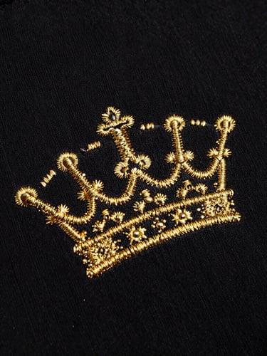 Close-up of premium heavy black cotton fabric texture, detailed gold embroidery of a crown, high-contrast dark lighting, sharp metallic reflections, 35mm
