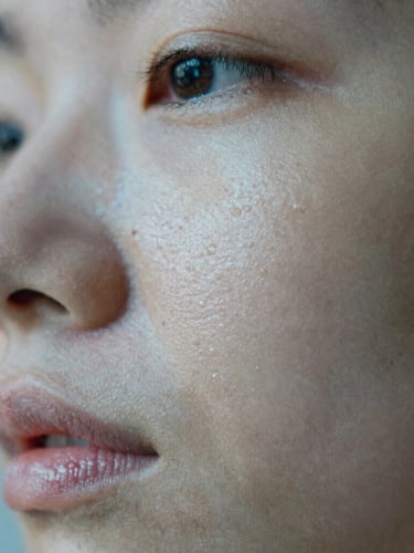 Macro close-up of healthy hydrated skin texture showing natural pores, soft morning light reflecting off clean glass, cool blue and warm gray tones, shallow depth of field