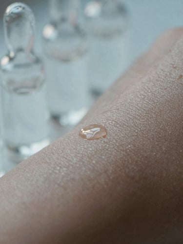 Macro photograph of healthy, hydrated skin texture with soft morning light reflecting off clean glass vials, cool blue and warm gray tones, shallow depth of field, 35mm.