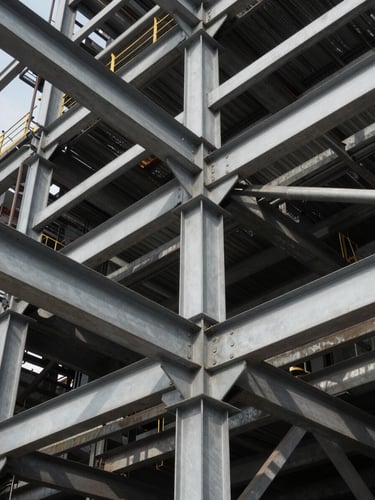 Low-angle heroic shot of complex structural steel connections of an industrial plant, high-contrast natural daylight, steel-gray tones with sharp shadows