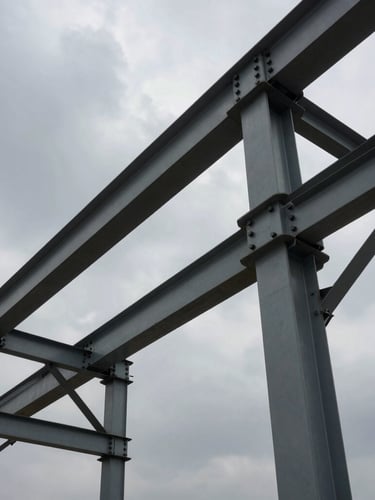 Low-angle hero shot of massive industrial steel framing structures under a dramatic overcast sky, highlighting heavy bolted connections and structural integrity.