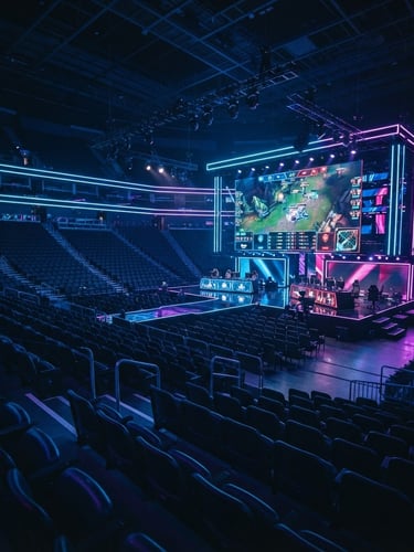 Wide shot of a modern esports arena with neon lighting, empty seats, and a large glowing screen displaying game statistics, low light, cinematic depth of field.