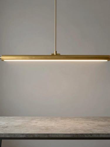 Symmetrical architectural composition, a matte brass linear pendant light casting soft warm illumination over a minimalist concrete table, diffused natural side-light.