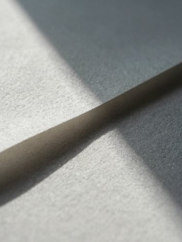 Extreme close-up of heavy structured cotton paper with sharp geometric shadows cast across the textured surface, cool daylight, architectural precision.