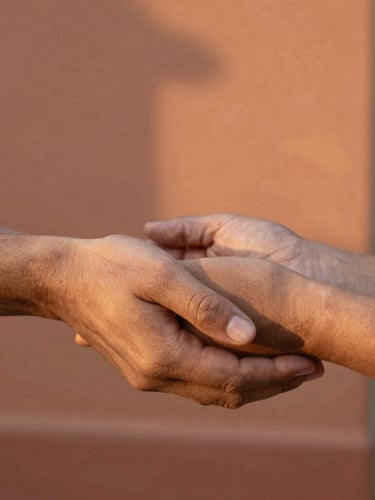 Close-up of hands holding warmly with a background of Jalisco terracotta clay walls, golden-hour natural light, shallow depth of field, authentic 35mm photography.
