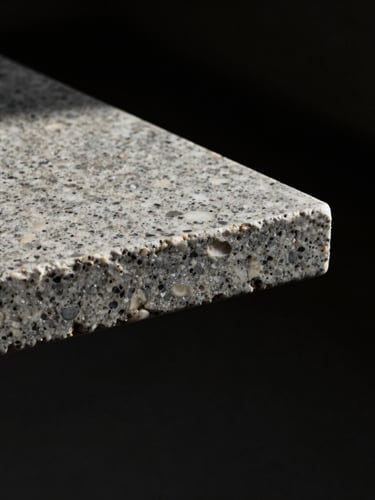 Close-up of a monolithic travertine table edge emerging from absolute black shadows, single-source natural light.