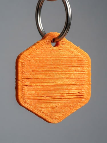 Macro photograph of a 3D printed orange keychain on a clean metal ring, sharp focus on the layer lines, bright side light, neutral gray background