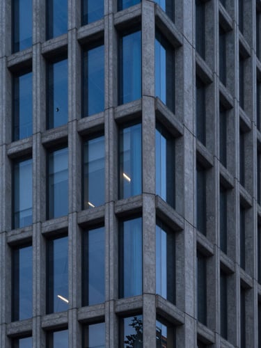 Sharp clean architectural lines of a modern steel and concrete skyscraper facade during twilight blue hour, high-contrast structural details