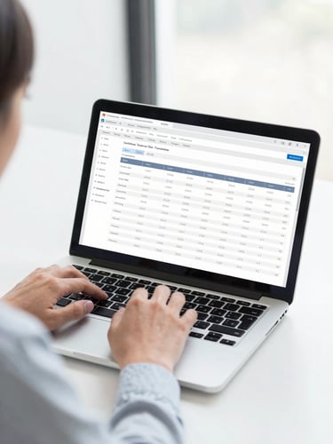 Bright high-key workspace photography, close-up over-the-shoulder shot of a financial controller working on a laptop, displaying clean financial tables, natural office daylight