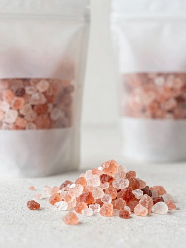 A serene eye-level portrait of raw pink Himalayan salt crystals alongside clean, minimalist packaging on a light stone surface, soft natural daylight, 35mm