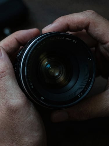 Extreme close-up of hands adjusting a vintage anamorphic camera lens, low-key dramatic lighting, high contrast, 35mm grain