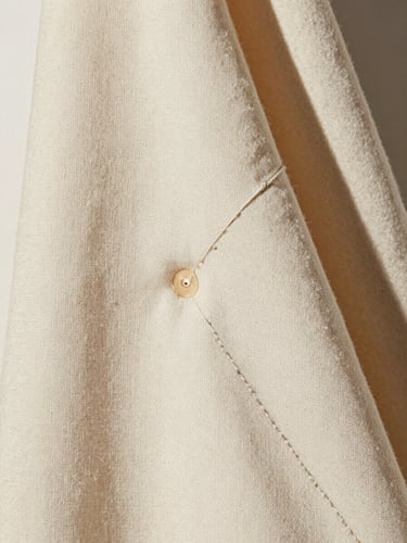 Macro detail shot of heavy cream linen drape, soft indirect daylight casting gentle shadows, showing precise double-needle stitching, portrait framing.