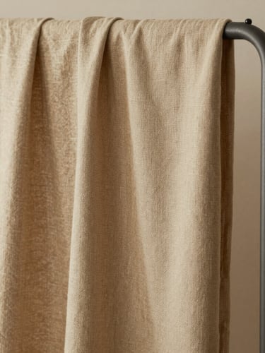 Close-up portrait of heavy linen fabric draping over a minimalist matte metal rack, soft indirect north-facing daylight, gentle shadows, warm camel beige tones.