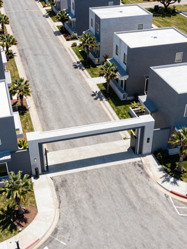 Sharp architectural drone photography of a gated township entrance, bright midday sun, clean concrete roads, modern boundary walls, 35mm