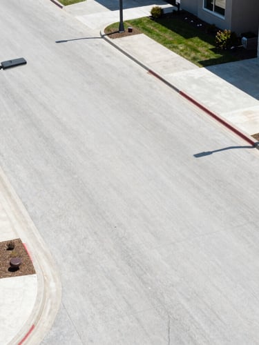 Close-up of newly paved wide concrete roads with modern streetlights and neat curbs in a premium gated community, bright daylight, 35mm