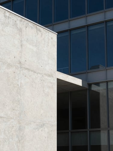 Minimalist architectural close-up of concrete and glass facades, sharp geometric shadows, high-contrast natural light, clean editorial framing.