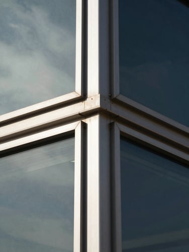 Sharp architectural photography of clean aluminum joints and structural curtain walls reflecting the sky under harsh desert sunlight, deep charcoal and metallic tones, 35mm lens