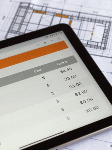 Close-up of a tablet screen displaying a detailed unit price analysis on a concrete construction site, architectural blueprints visible in the background, sharp daylight