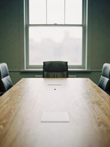 Quiet corporate boardroom with a large wooden table, empty leather chairs, soft natural window light, low contrast, editorial documentary style.