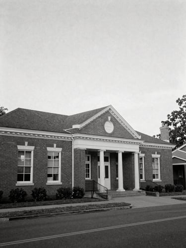 A black and white documentary photograph of a historic brick community center under soft daylight, wide environmental framing, 35mm lens.