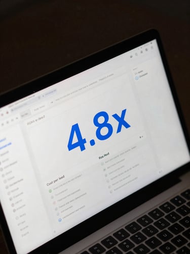 Overhead close-up of a laptop screen displaying an ad campaign dashboard — ROAS metric at 4.8x highlighted in electric blue, cost-per-lead column visible, dark interface, studio strobe lighting, tight crop, no person visible