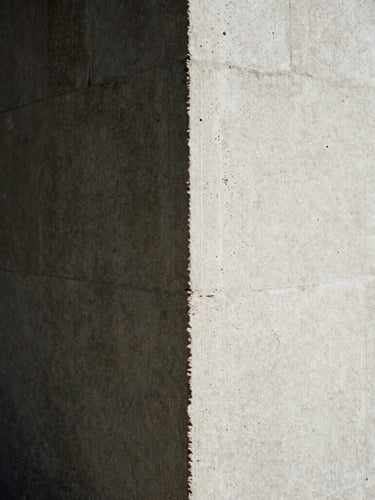 Grainy 35mm close-up of harsh sunlight hitting a raw concrete pillar, deep architectural shadow, minimalist high-contrast composition