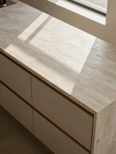 Overhead architectural study of a modular kitchen island in honed stone and brass-pull cabinetry, natural north-facing light from a skylight above creating even shadows across the surface, premium hardware detail visible, no people, no clutter