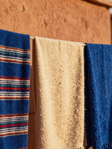 Close-up of hand-woven Berber wool textiles drying in the sun against a terracotta wall, rich textures, warm golden hour light, shallow depth of field