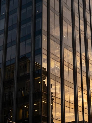 Warm editorial corporate photography, soft window light reflecting on modern glass facade of a São Paulo office building, deep navy and gold tones, 35mm
