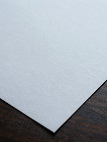 Macro detail of high-end textured paper documents on a clean dark oak desk, soft overcast daylight, cool shadows, sharp focus