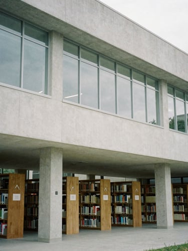 Modern university library with clean architectural lines, concrete and glass, quiet research environment, desaturated academic tones, 35mm.