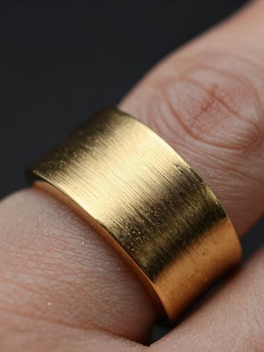 Extreme macro close-up of a heavy-gauge gold ring on a finger, focusing on the brushed champagne texture and sharp architectural edges under dramatic low-key lighting.