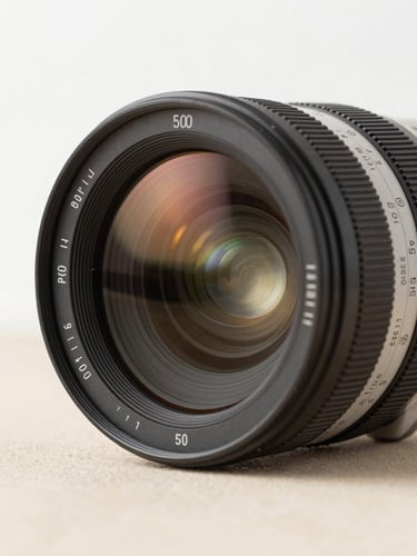 Close-up of a professional cinema camera lens reflecting warm studio light, clean white and sand background, sharp focus, 50mm
