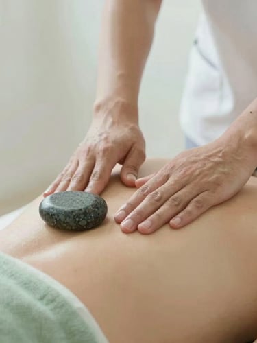 Close-up of professional therapist hands performing precise massage technique on a back, warm basalt stones nearby, soft natural light, shallow depth of field