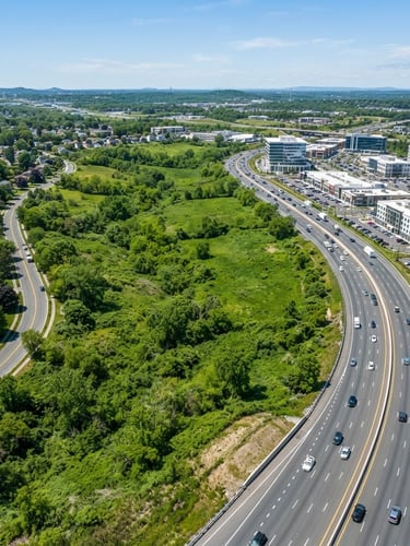 High-angle drone photography of a lush green strategic land parcel adjacent to a modern highway and commercial development, bright natural daylight, editorial architectural style