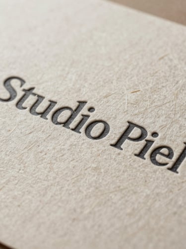Close-up of heavily textured handmade paper with embossed Studio Piel branding, soft side lighting highlighting the fiber details