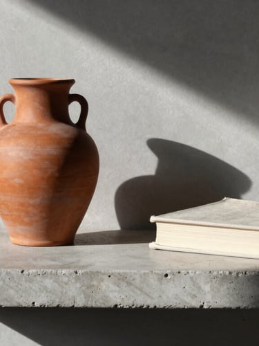 A minimalist concrete shelf holding a terracotta vessel and a single linen-bound book, soft morning light casting long diagonal shadows.