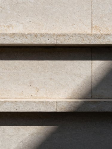 Extreme architectural close-up of a travertine stone facade, sharp geometric shadows from direct sunlight, minimalist composition.