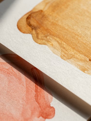 Extreme close-up of textured paper mockups layered with vibrant amber and soft coral ink, sharp shadows from warm natural sunlight.