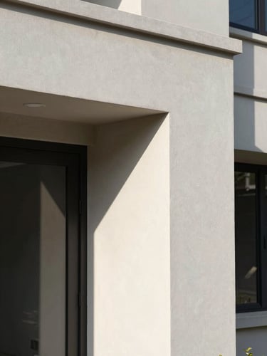 Close-up of a completed residential building entry facade in full daylight, clean plastered wall surface with recessed door frame, architectural shadow lines, no people, sharp detail, natural light