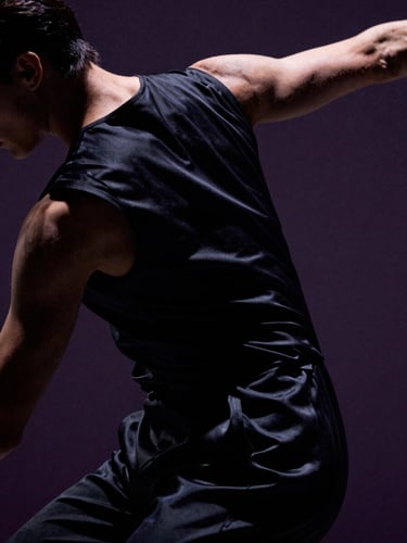 Cinematic close-up of a dancer's back in tense motion, draped in structured black silk, dramatic chiaroscuro lighting, deep shadows, 35mm anamorphic lens.