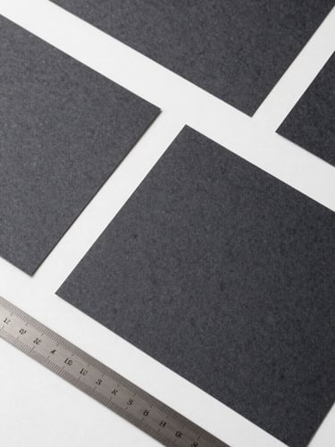 Strict top-down flat-lay of modern brand collateral, heavy charcoal paper stocks, and precise steel rulers on a white surface under cool daylight.