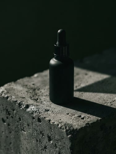 Matte black serum bottle resting on a raw concrete block, dramatic low-key side-lighting casting a sharp geometric shadow, extreme close-up, wide aspect.