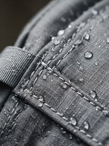Macro close-up of heavy-duty technical backpack stitching, water droplets on textured ripstop nylon, bright crisp daylight, sharp detail, 50mm