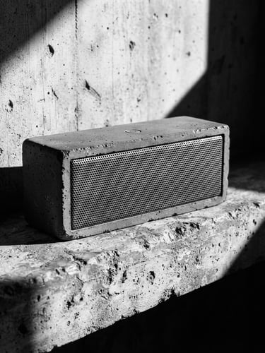 Stark industrial product photography, harsh architectural side-lighting, a monolithic concrete wireless speaker on a raw concrete ledge, sharp shadows, 50mm lens