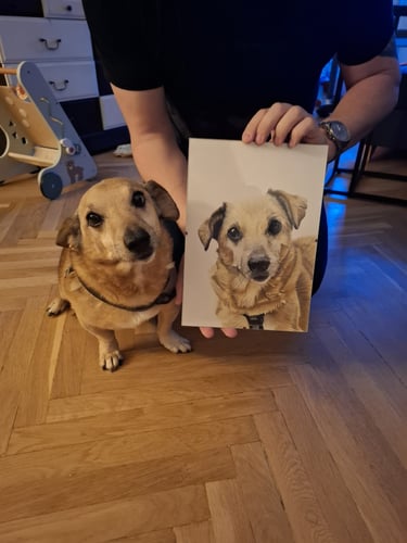 A small cream mixed breed dog sitting next to its framed custom dog portrait.