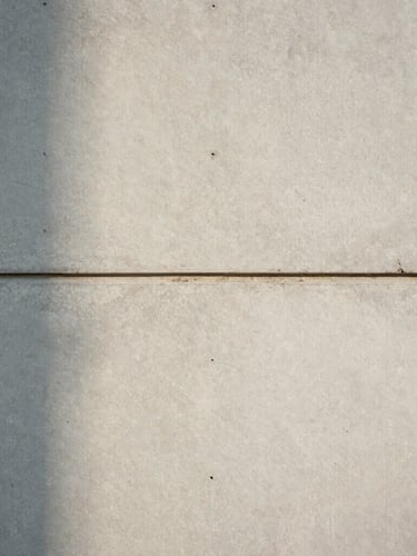 Straight-on architectural elevation of a concrete and honed travertine wall joint, soft natural daylight casting subtle shadows, minimal spatial composition.
